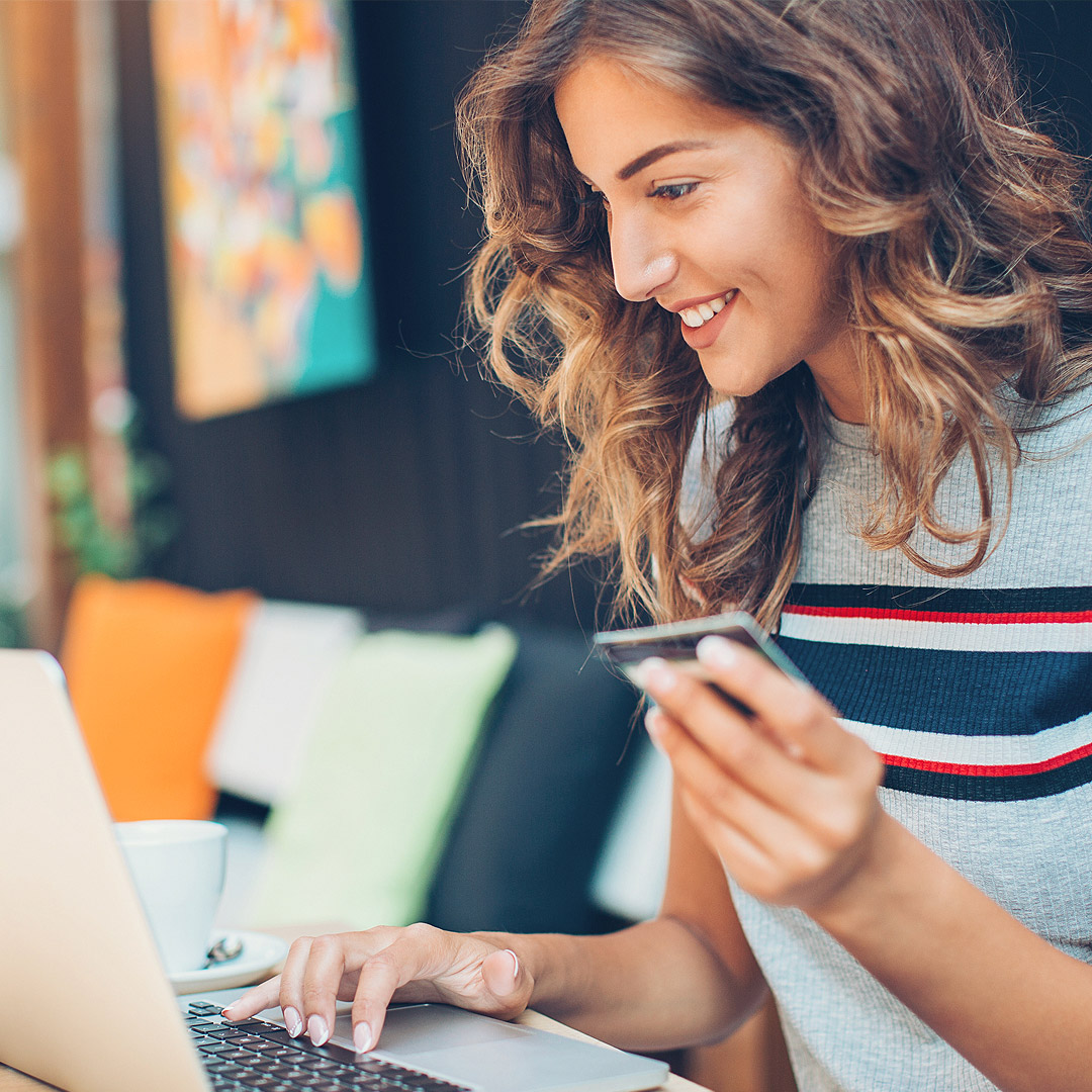 woman smiling at computer holding credit card