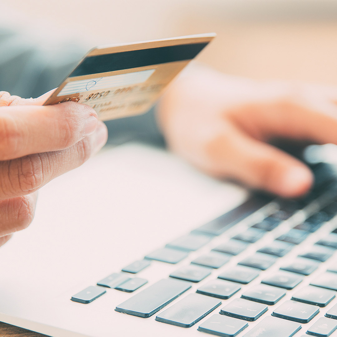 credit card with hand holding it over close up of computer keyboard